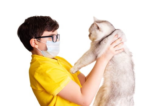 A brunette boy in glasses and medical mask, in yellow t-shirt, holds his white cat, isolated on white background. Allergy to animal fur concept. Close up. Copy space