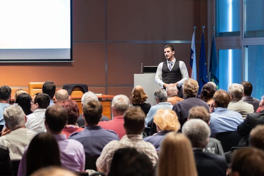 Speaker giving a talk in conference hall at business meeting event. Rear view of unrecognizable people in audience at the conference hall. Business and entrepreneurship concept.