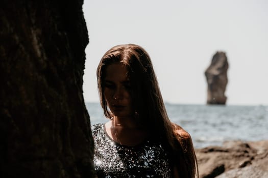 Woman travel sea. Young Happy woman in a long red dress posing on a beach near the sea on background of volcanic rocks, like in Iceland, sharing travel adventure journey