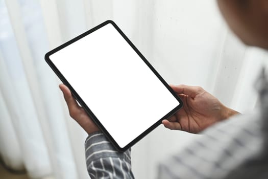 Closeup over shoulder view man holding digital tablet standing in bright office. Blank screen for your advertising text message.