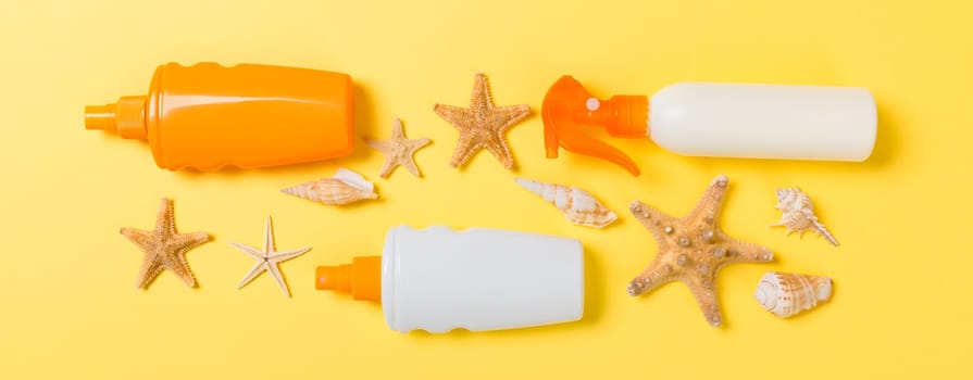 Sunscreen bottles with seashells on yellow wooden table.