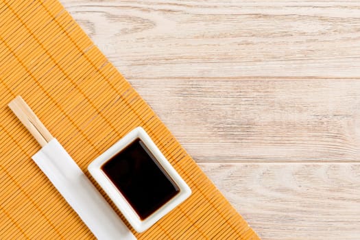 Bamboo mat and soy sauce with sushi chopsticks on wooden table. Top view with copy space background for sushi. Flat lay.