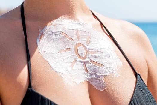 Sun shaped sunscreen on woman's breast over sea background.