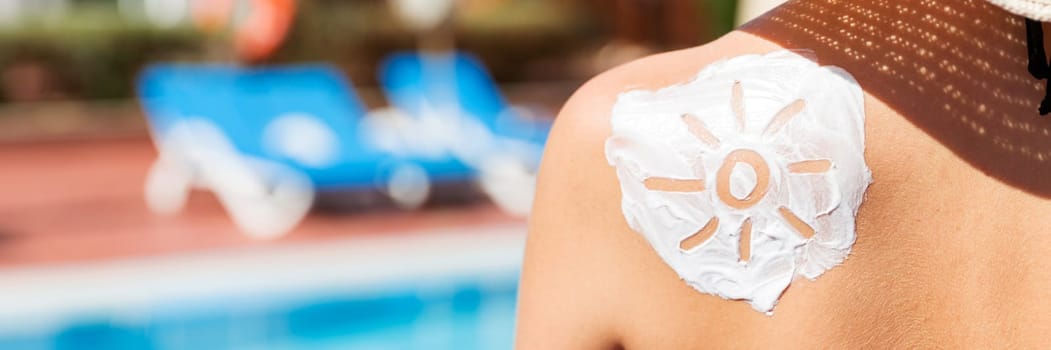 Beautiful woman with drawn sun by sun cream on her shoulder by the pool. Sun Protection Factor in vacation, concept.