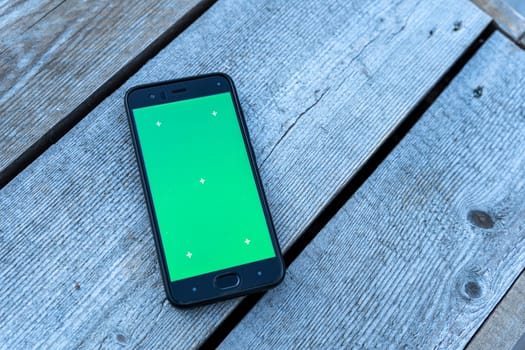 a smartphone with a green screen lies on a faded wooden background. chromakey, mockup. mobile phone app advertising