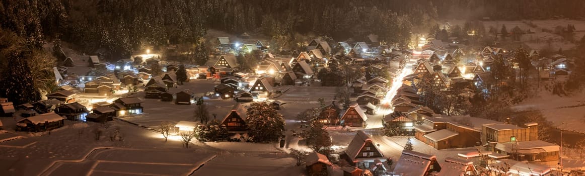 Panoramic view of snow and mist falling on traditional Japanese mountain village at night. High quality photo