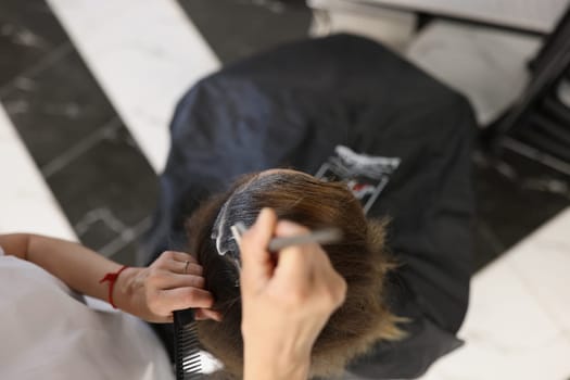 Hairdresser dyes hair of woman in beauty salon. top view. Hair coloring service in barbershop concept