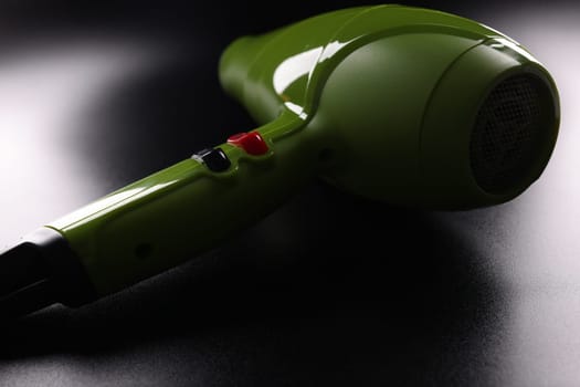 Green modern hair dryer with buttons on dark background. Choosing a hair dryer for hair styling concept