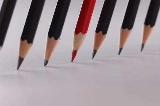 Bright red pencil stands out from identical black pencils. Different concept of teamwork and business success