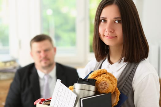 Boss fires young woman from office job. Fired woman with box of things in office