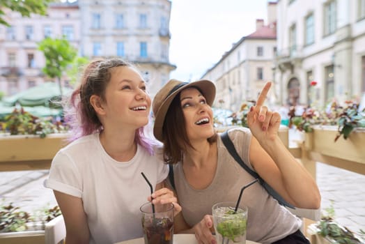 Two women mother and teenage daughter sitting in city outdoor cafe talking, drinking summer ice cold drinks, mojito, cocktail