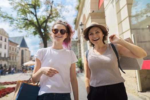 Happy smiling mother and teenage daughter walking together with shopping bags. Beauty, fashion, parent child communication, positive emotions. Sunny day in city, summer discounts and sales