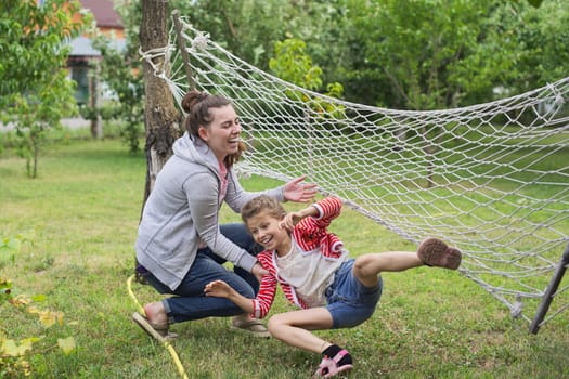 Child girl falling from hammock, spring garden background, having fun laughing girls