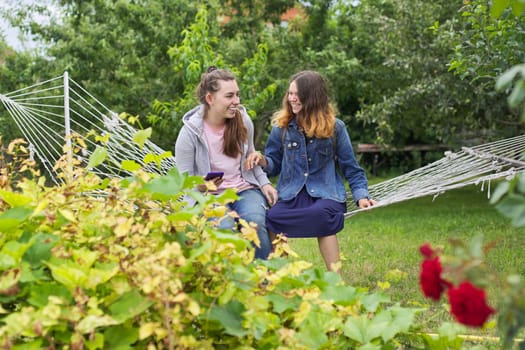 Two teenage girls having fun laughing on a hammock in a garden