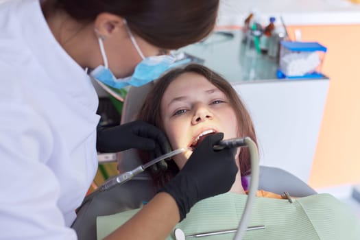 Woman doctor dentist treating teeth to girl patient in dental office. Dentistry, healthy teeth, medicine and healthcare concept