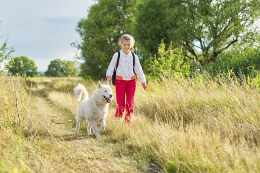 Little girl running with dog in meadow. Child playing with pet in nature, healthy active lifestyle of children, friendship of animals and humans