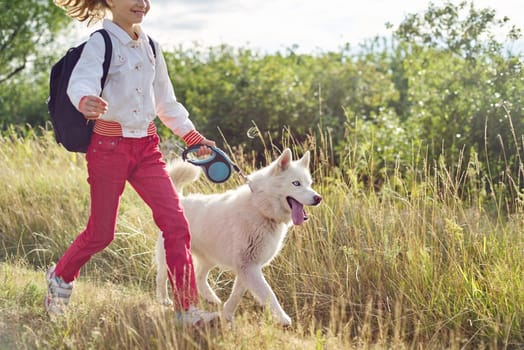 Little girl running with dog in meadow. Child playing with pet in nature, healthy active lifestyle of children, friendship of animals and humans