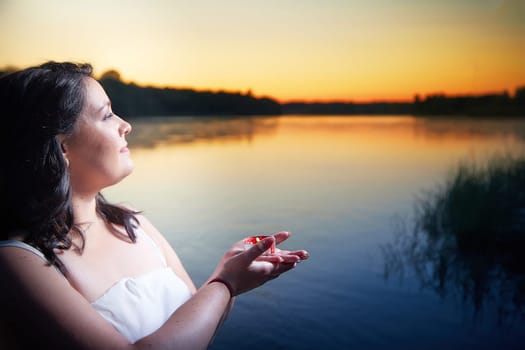 Slavic plump plump chubby girl in long white dress on the feast of Ivan Kupala with flowers and water in a river or lake on summer evening