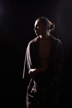 The silhouette of a girl in a veil looking like a statue or sculpture on black background. A model poses for a photo shoot in the studio