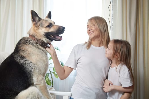 Happy loving family with mother, daughter and big dog in living room. Pet chephers, woman mom and small child girl who is afraid of a dog taken from a shelter