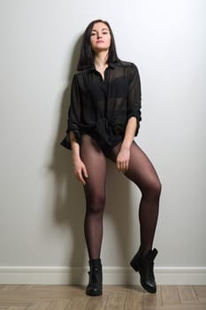 Fashionable young beautiful woman in black nylon tights, stylish leather boots and black blouse