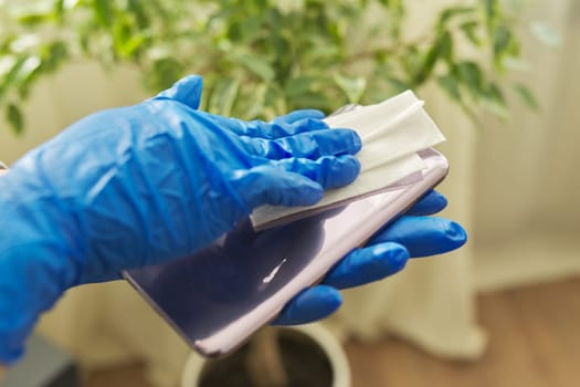 Prevention of the spread of coronavirus infection . Close up of hands in rubber gloves disinfecting mobile phone