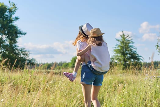 Happy children two girls sisters teenager and younger laughing and having fun in meadow, blue sky, summer nature. Active healthy lifestyle, friendly family, happy childhood, copy space
