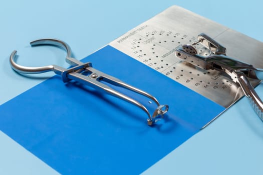 Dental hole punch, the metal plate, the rubber dam and the rubber dam forceps on the blue background. Medical tools concept.