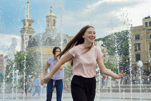 Teenage girls, people having fun in the city fountain, splashing, wet clothes, positive emotions