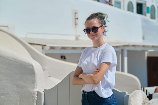 Teenager girl resting on Greek island Santorini, female looking at camera, background white architecture of village Oia, copy space