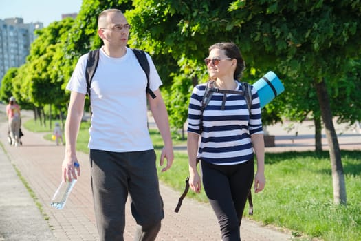 Talking middle-aged man and woman, couple walking along park road for sports fitness training, active healthy lifestyle and relationships of age 40 years old people