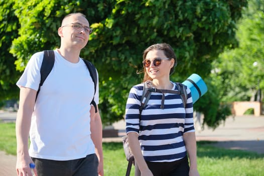 Talking middle-aged man and woman, couple walking along park road for sports fitness training, active healthy lifestyle and relationships of age 40 years old people