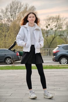 Outdoor portrait of smiling teenage girl of 14, 15 years old in jacket on spring street.