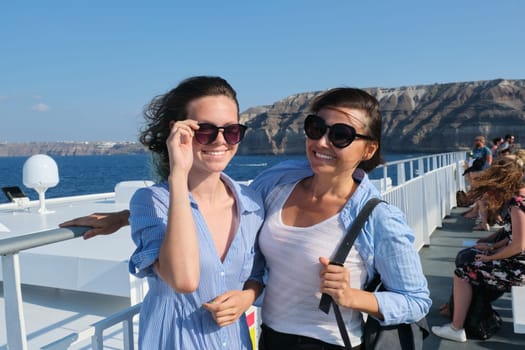 Passenger shipping, mother and teen daughter on deck of ferry. Happy family trip, background Greek island Santorini sea sky, golden hour