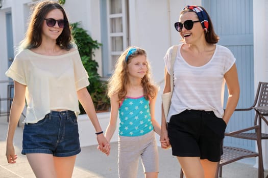 Mother and two daughters teenager and youngest walking together holding hands. Friendly family, happy parent and children, summer resort landscape background