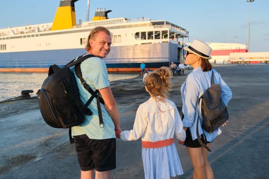 Sea family vacation, mother father and daughter child in seaport holding hands looking at the ferry