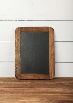 Close up empty blank black slate chalkboard sign over white wooden painted wall on table
