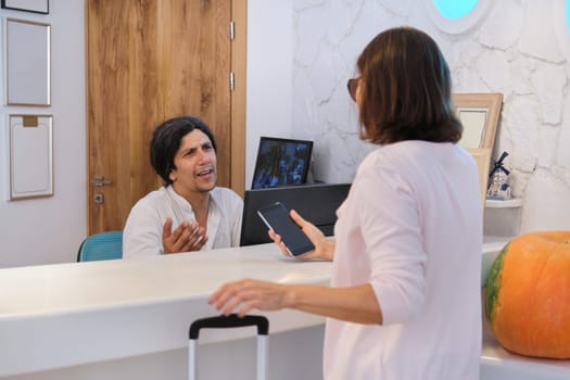 Resort hotel front desk, woman guest talking to man working at reception.