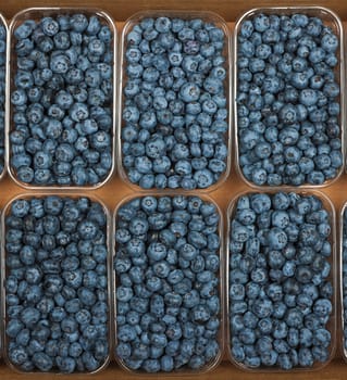 Close up several plastic containers of fresh ripe blueberry berries in brown cardboard box on retail display, elevated top view, directly above