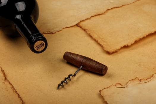 Close up one full unopen bottle of red wine with cork and retro opener with wooden handle over vintage brown paper background with copy space, high angle view
