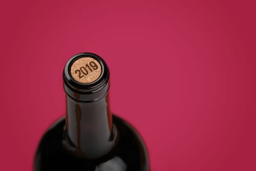 Close up one full unopen bottle of red wine with cork over burgundy purple background with copy space, high angle view, vintage 2019 year