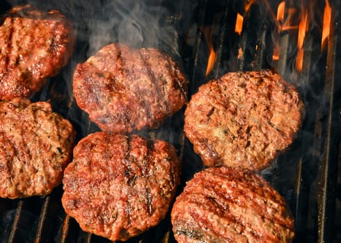 Close up searing and smoking beef or pork meat barbecue burgers for hamburger on bbq fire flame grill with cast iron metal grate, high angle view