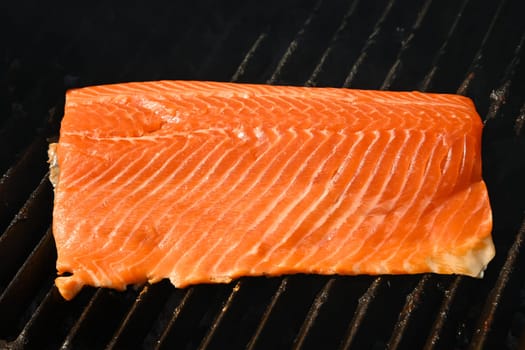 Close up searing and smoking salmon fish fillet on open fire outdoor grill with cast iron metal grate, high angle view