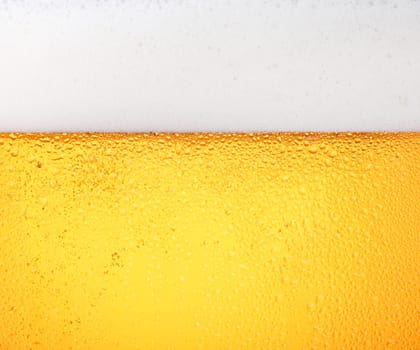 Close up background texture of pouring lager beer with bubbles and froth in frosty glass with drops, low angle side view