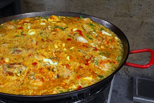 Close up cooking traditional Spanish Valencian mixed paella with chicken, seafood and vegetables in big frying pan, high angle view