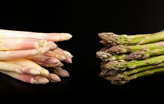 Close up two bunches of fresh white and green asparagus compared isolated on black background, high angle view