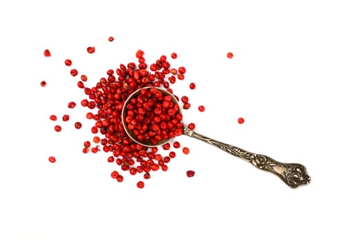 Close up one vintage metal spoon full of red pink pepper peppercorns spilled and spread around isolated on white background, elevated top view, directly above