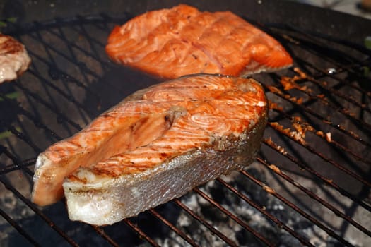 Close up cooking salmon fish steak and fillet on on bbq grill grate, high angle view