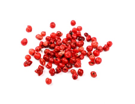 Close up heap of red pink pepper peppercorns spilled and spread around isolated on white background, high angle view