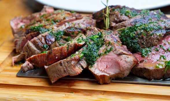 Close up big portion of sliced grill roasted beef chateaubriand tenderloin meat with thyme and herbs served on wooden cutting board, high angle view